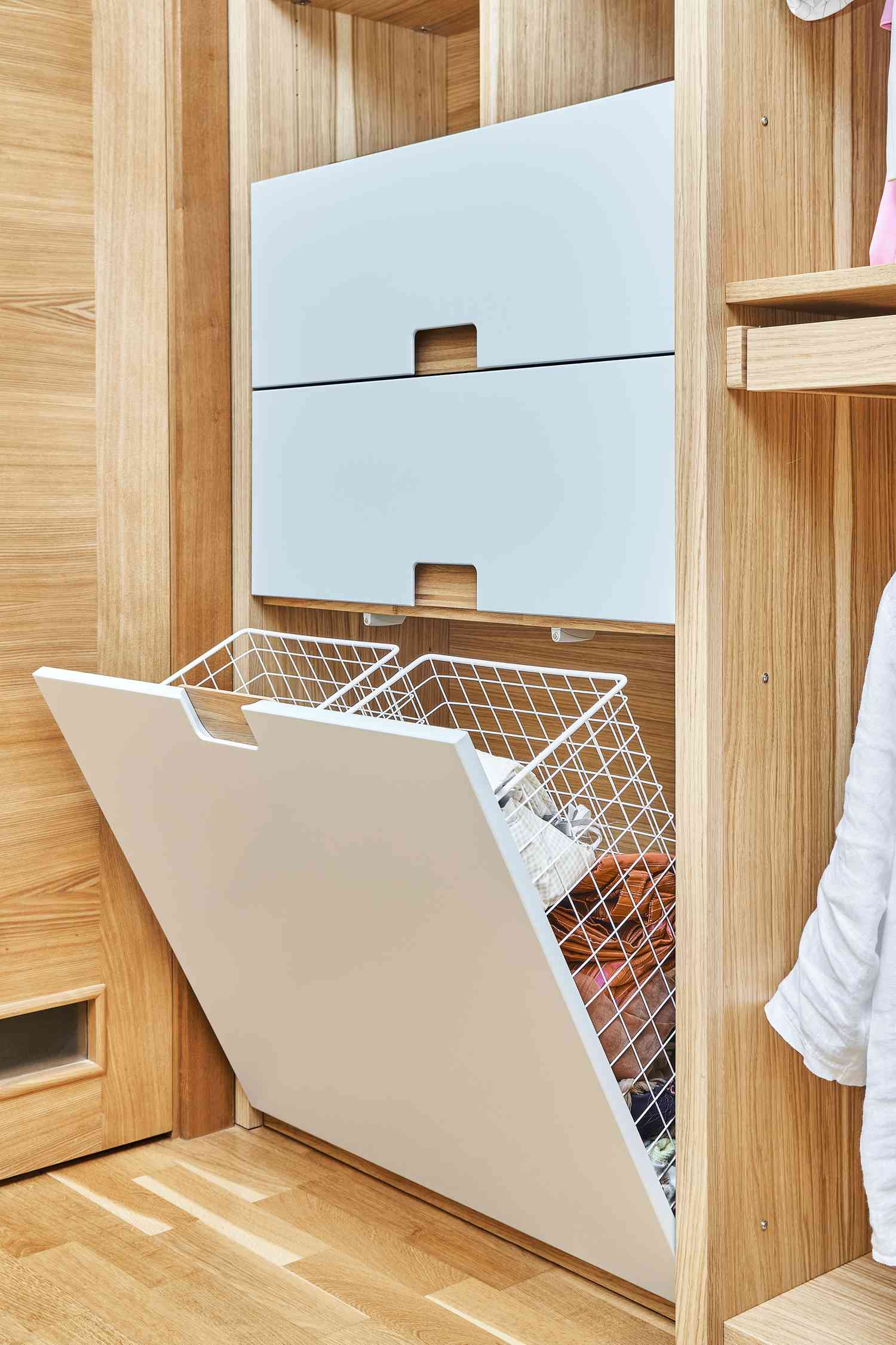 Modern wardrobe with opened metal mesh laundry basket and wooden drawers. Wooden wardrobe with flat finger pull wardrobe doors. Oak veneered plywood cabinets with light gray painted cabinet doors