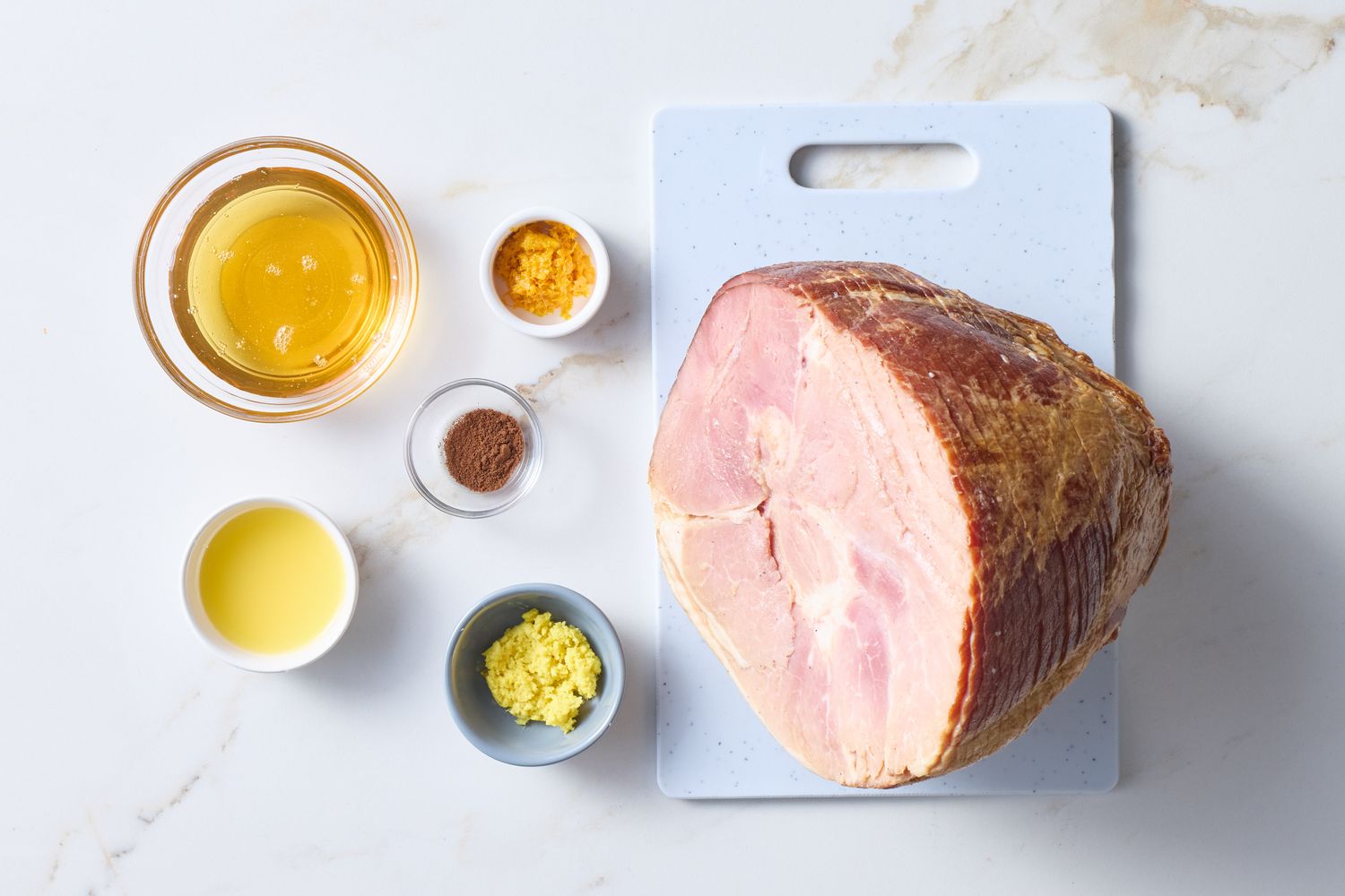 A selection of ingredients including a ham bowls of liquids spices and zest on a countertop