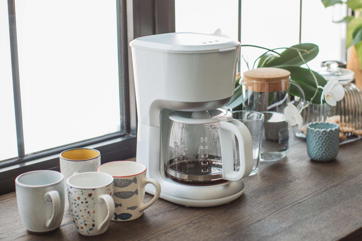 Coffee maker with a pot of coffee on a counter surrounded by mugs and kitchen items