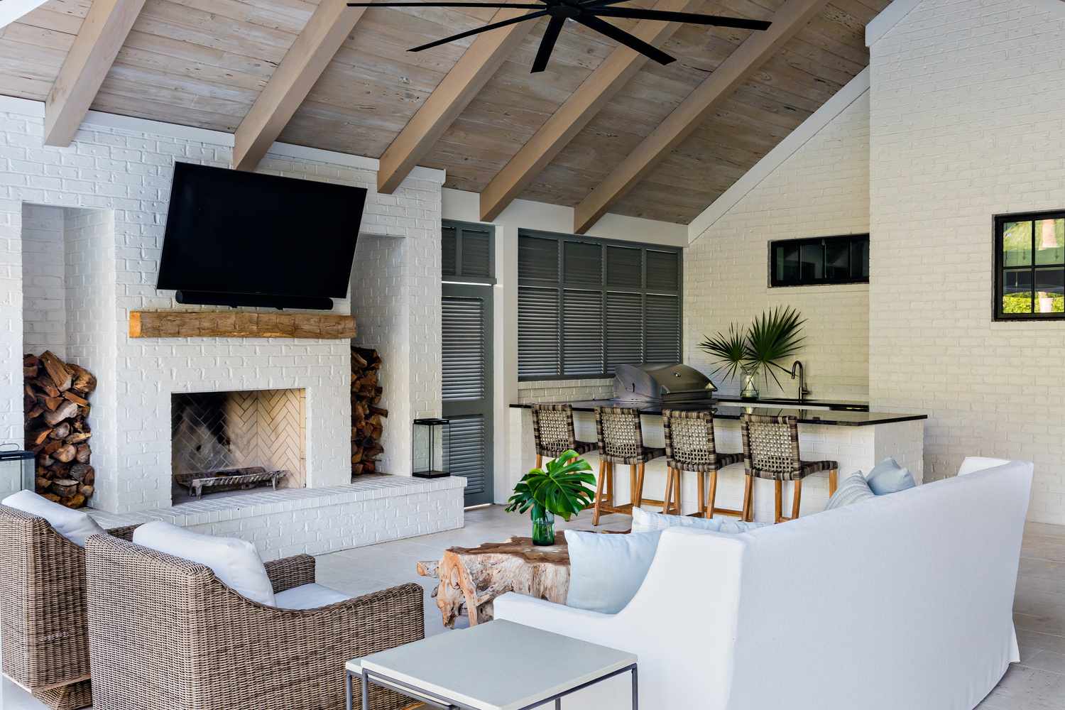 a covered outdoor area with plush seating, woven accents, and a wood burning fireplace
