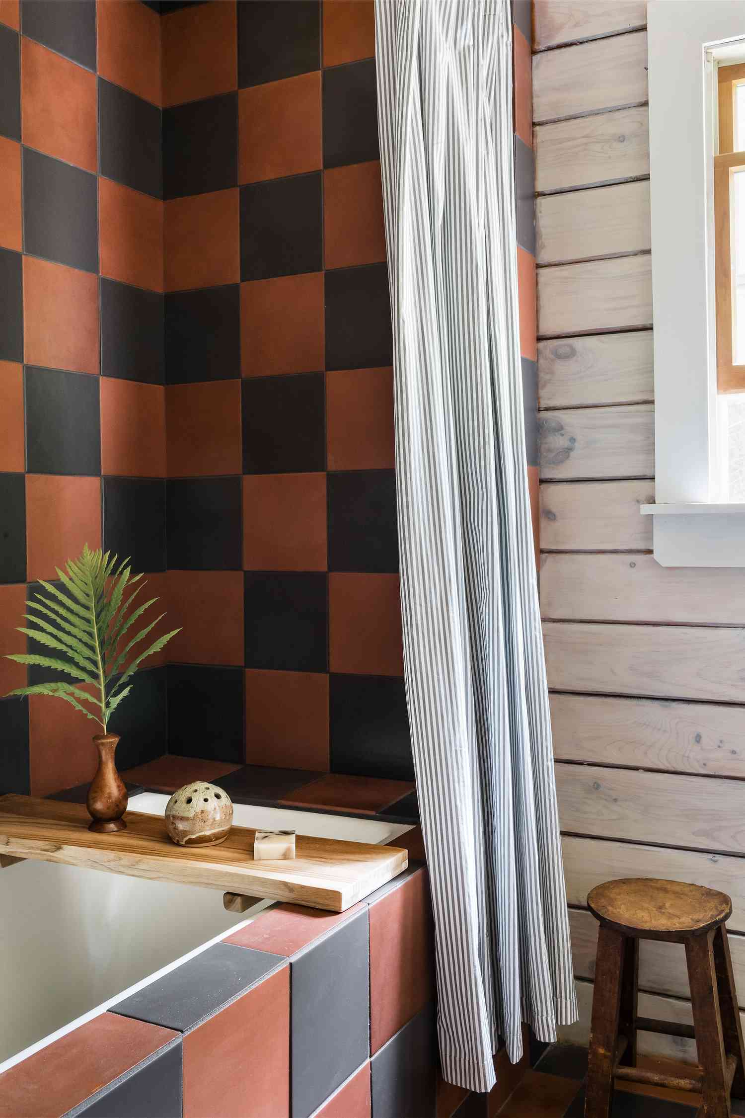 Bathroom with a square-patterned tiled wall, wooden stool, and a vase with foliage