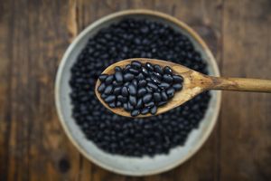 Wooden spoon holding black beans over a bowl filled with black beans