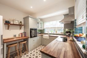 A modern kitchen with a wooden countertop tiled floor and appliances featuring a small dining area with two stools