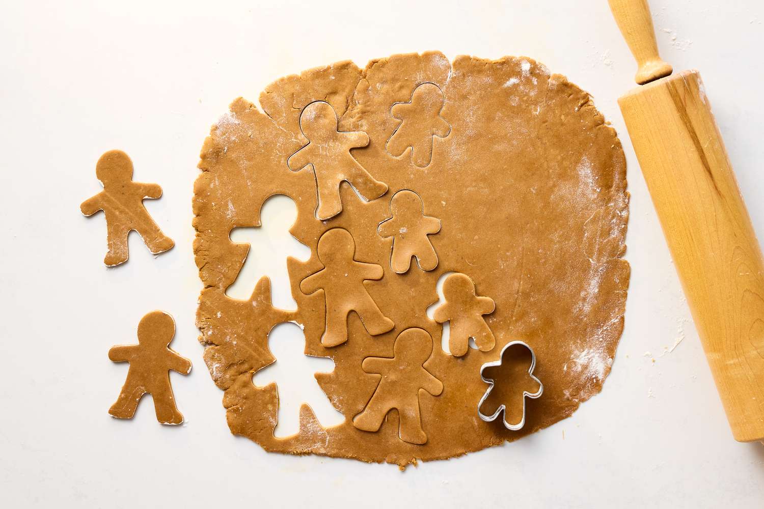 Gingerbread dough rolled out with cookie cutouts shaped as gingerbread people next to a rolling pin on a table