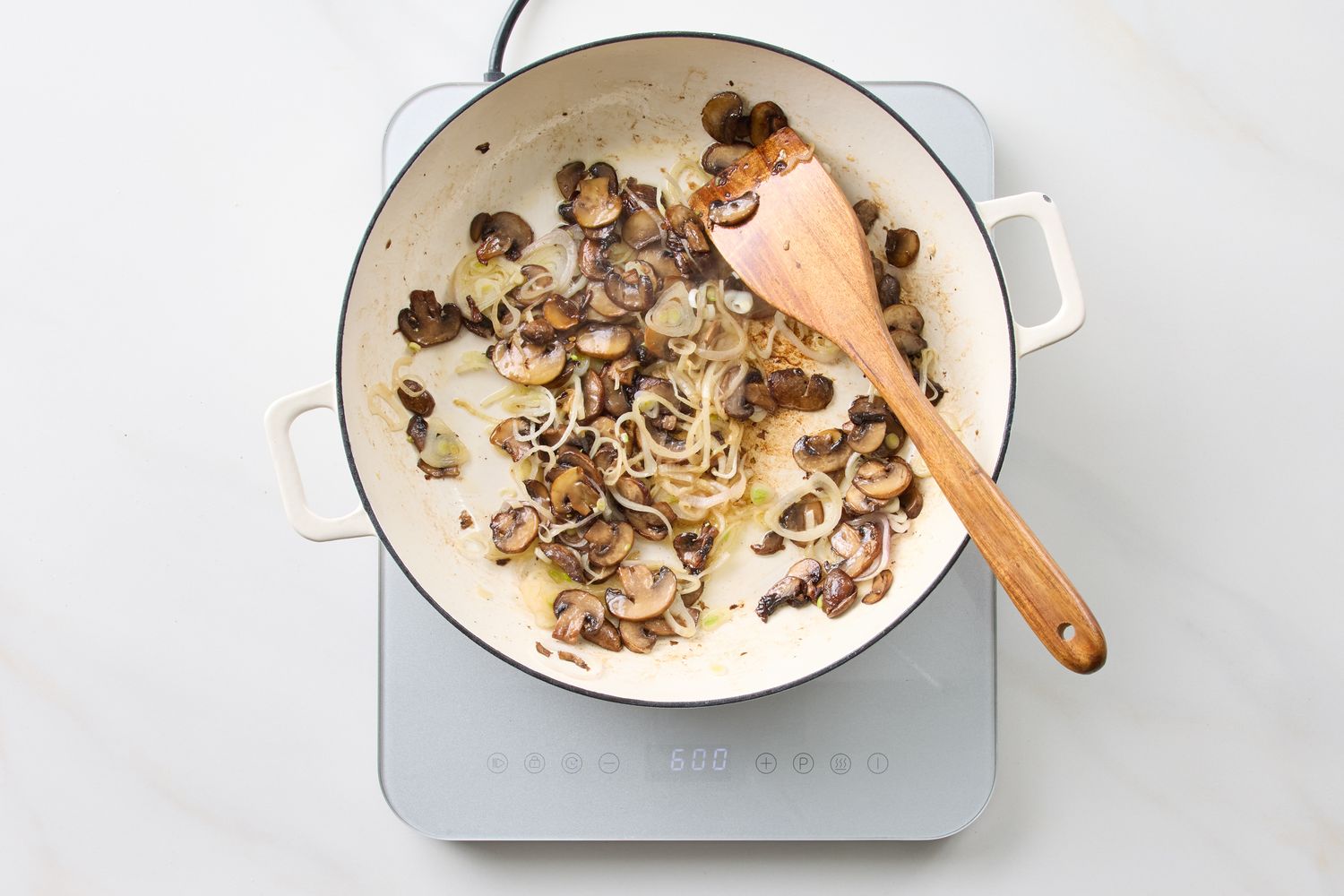 Pan containing cooked mushrooms onions and a wooden spatula on a stovetop