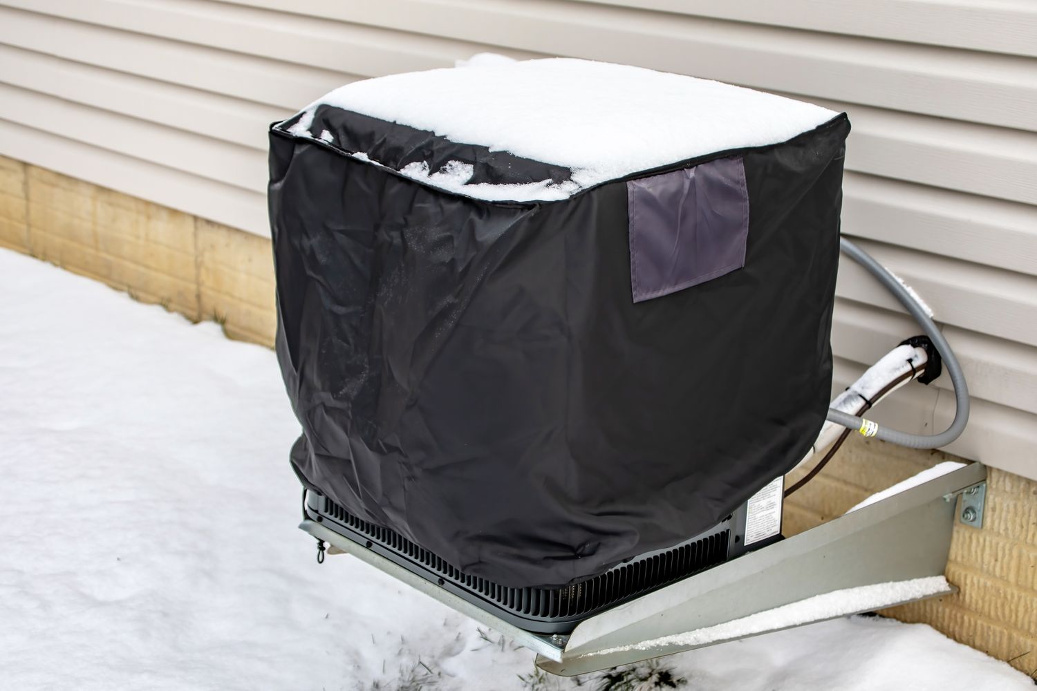 An outdoor HVAC unit covered with a protective cover surrounded by snow