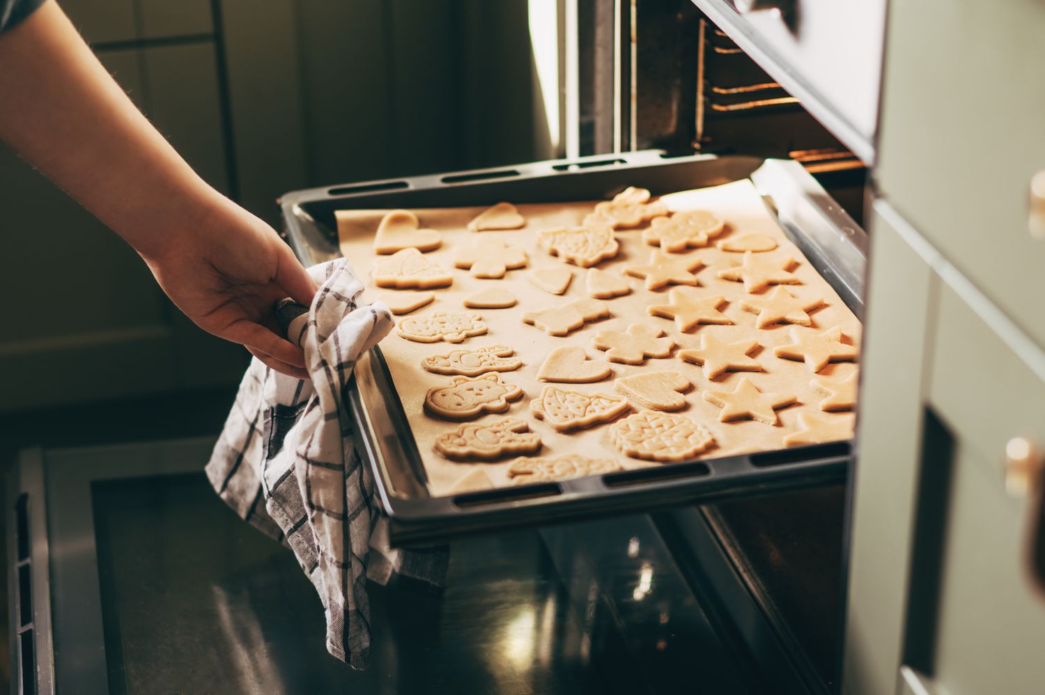 A person placing a tray of shaped cookies into an oven