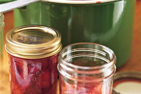 Jars of strawberry preserves next to a green pot filled with preserves with a ladle resting inside