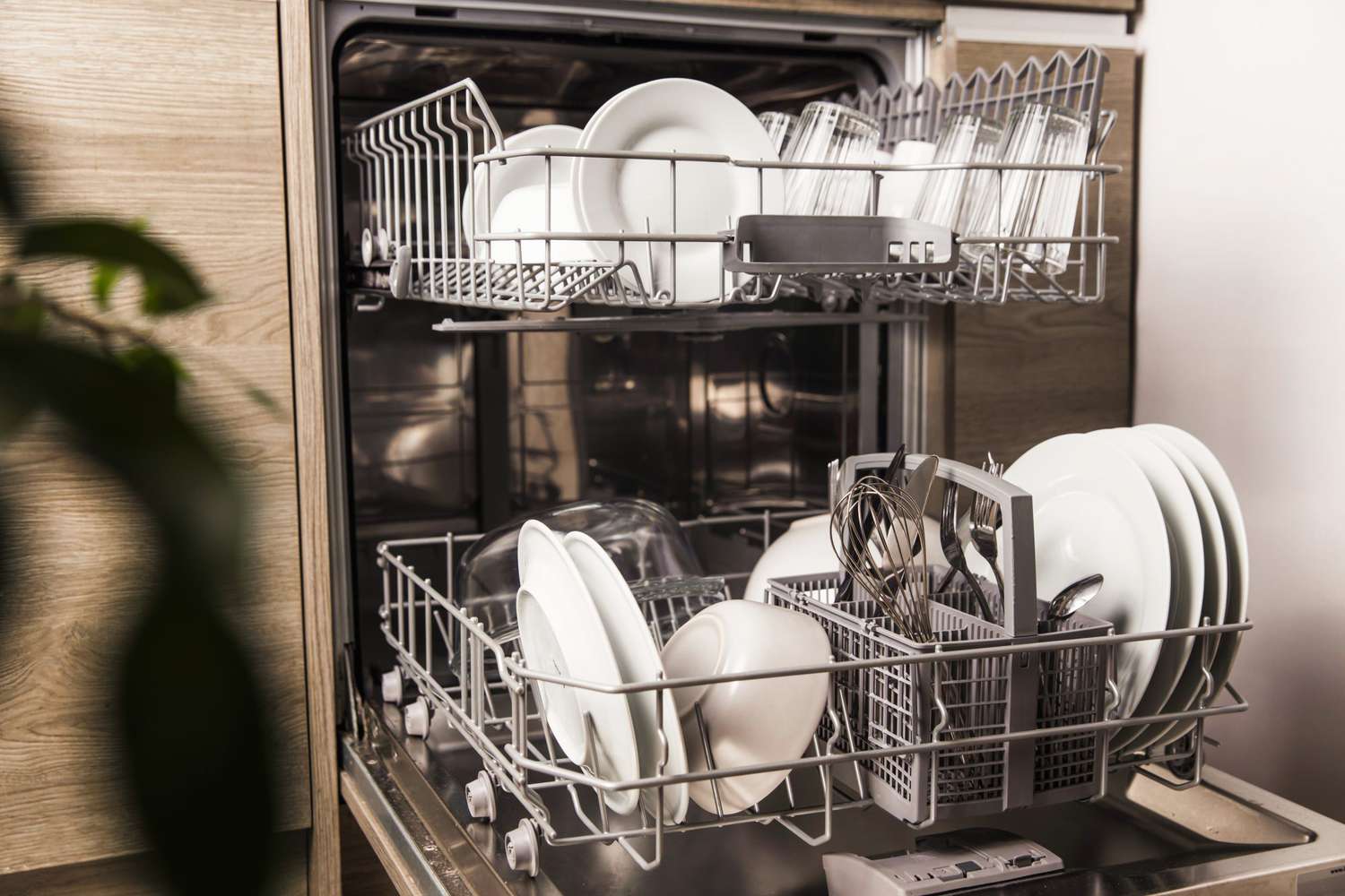Open dishwasher with clean utensil inside, cutlery, glasses, dishes at kitchen