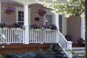 A front porch with hanging and railing flower baskets white railing and a few chairs visible