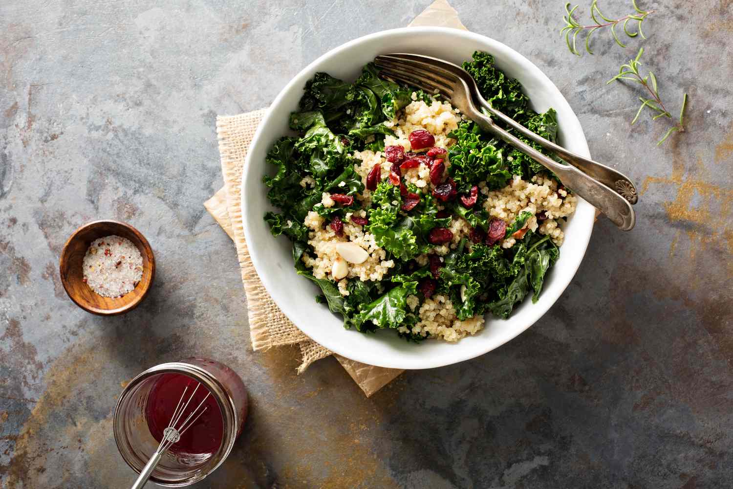 kale and quinoa in white bowl with cranberries and 2 forks