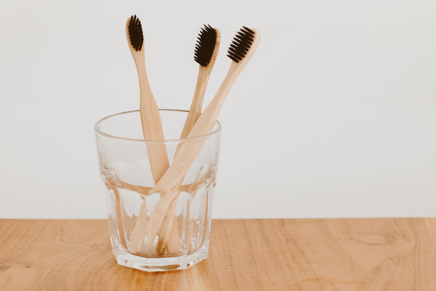 Three wooden toothbrushes in a glass on a tabletop