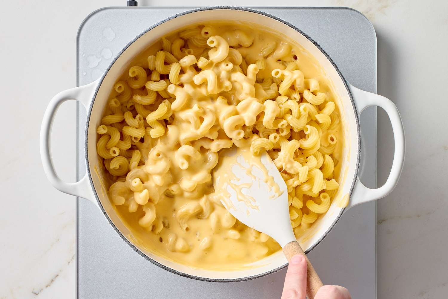 Macaroni and cheese being stirred in a pot with a white spoon