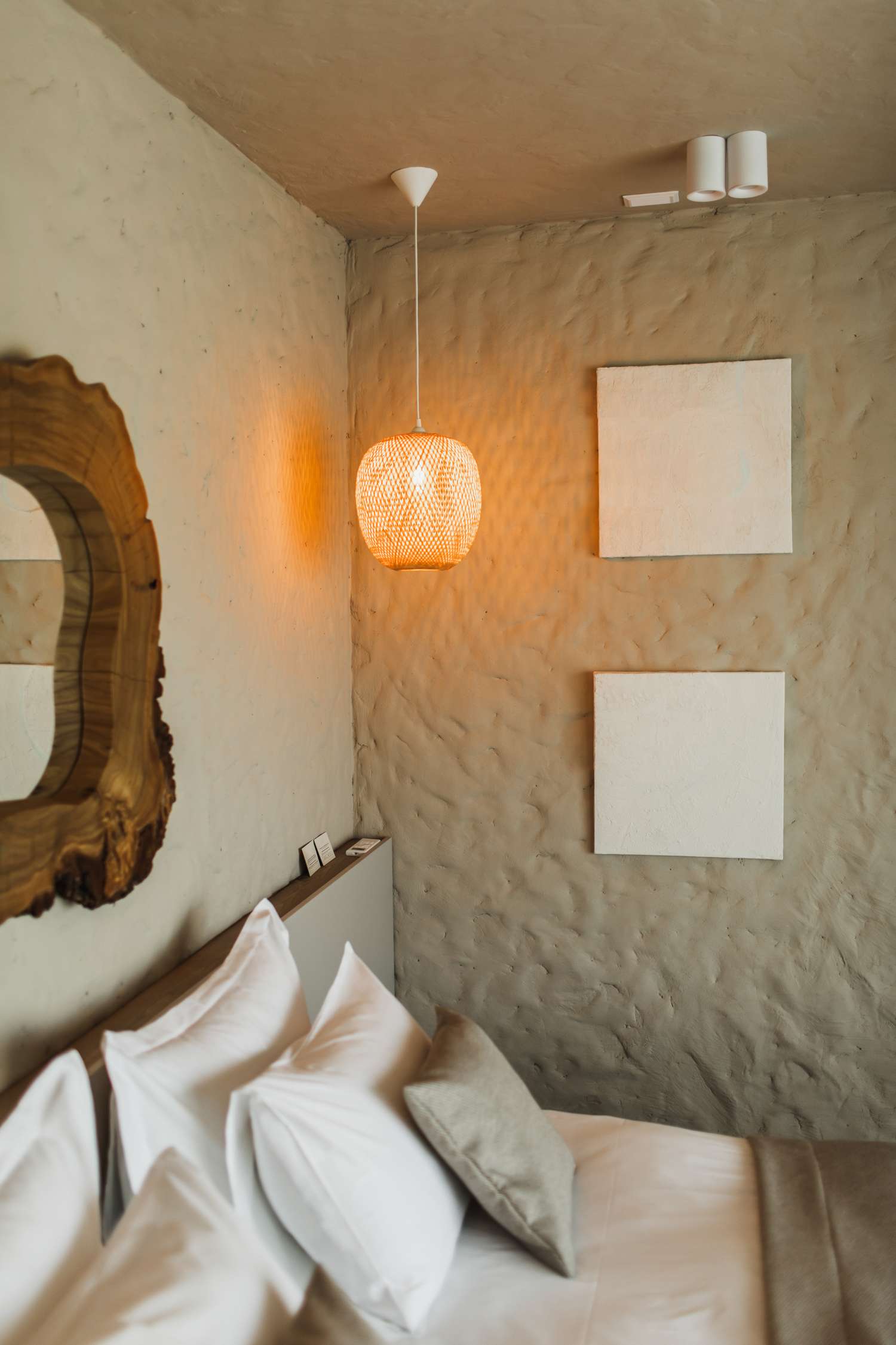 A cozy bedroom corner with pillows on a bed textured wall decorative mirror pendant light and two square wall decorations