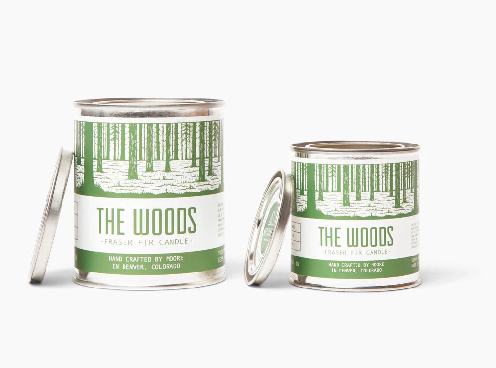 Two tin containers labeled The Woods Fraser Fir candles one large and one small with lids resting nearby