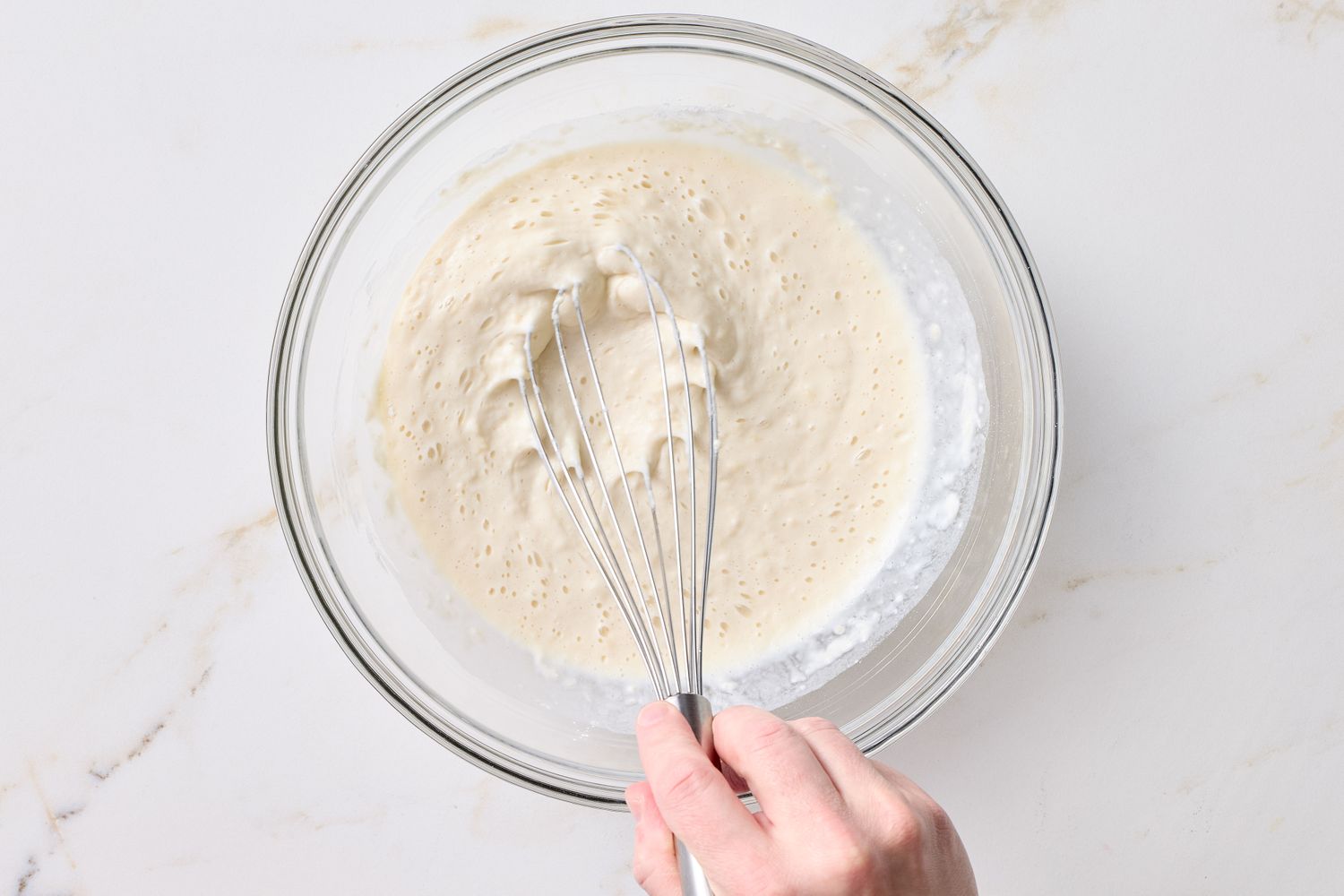 Hand whisking a batter in a glass bowl