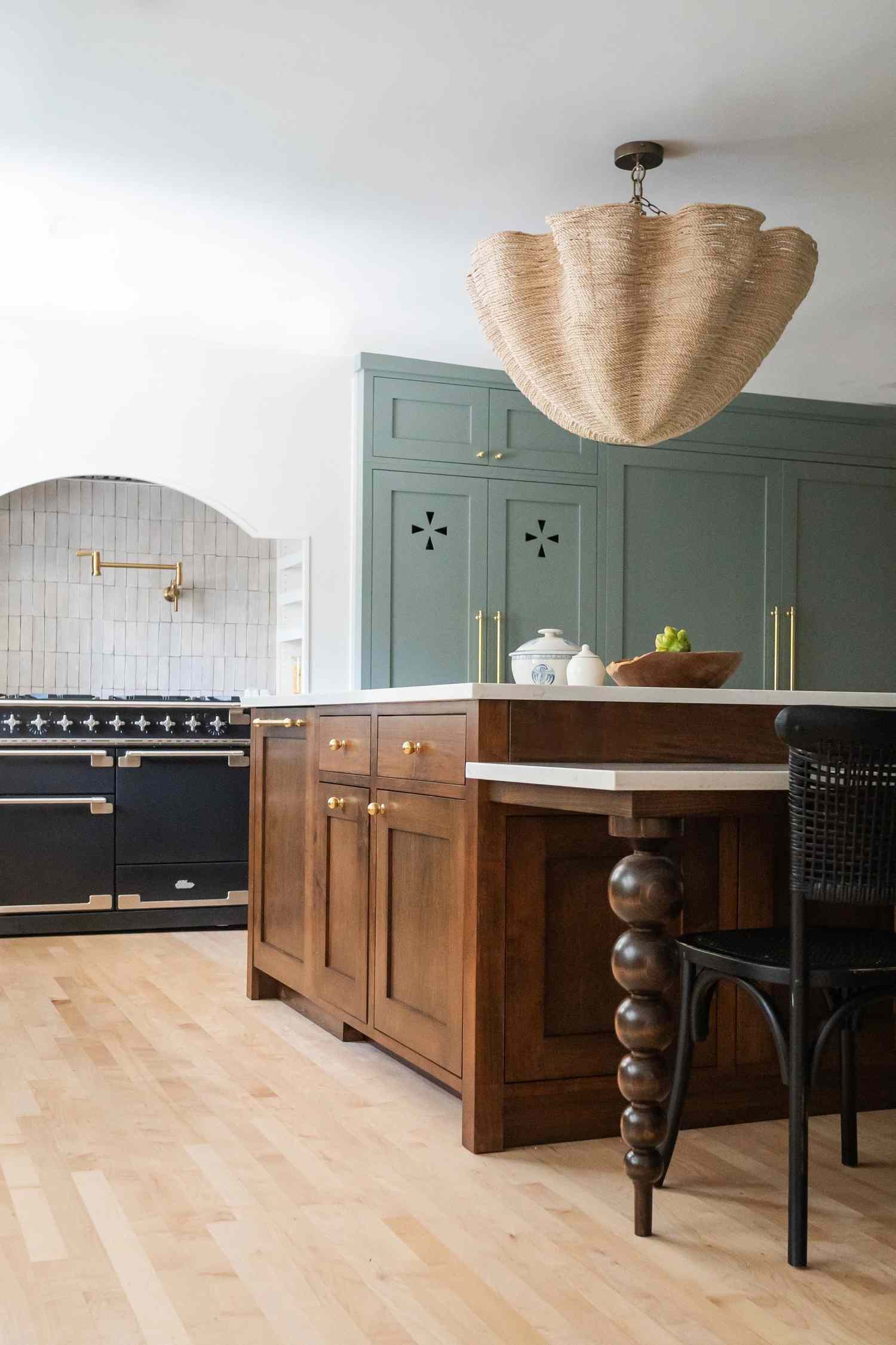 A modern kitchen featuring a wooden island a black range stove and green cabinets adorned with a unique pendant light