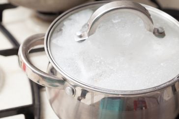 Cooking pot with lid foaming from boiling liquid on stovetop