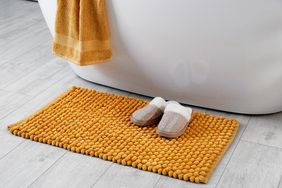 A soft bath mat and slippers placed near a bathtub