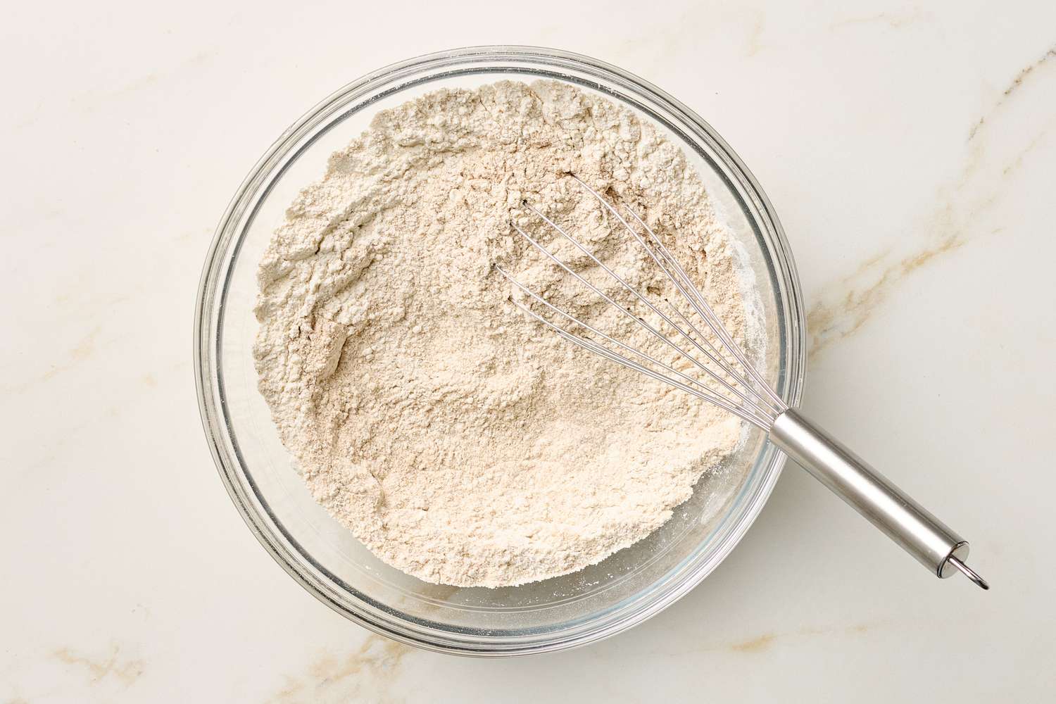 A bowl of dry ingredients with a whisk on a countertop