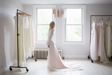 A woman in a bridal gown standing in a showroom with other dresses on racks