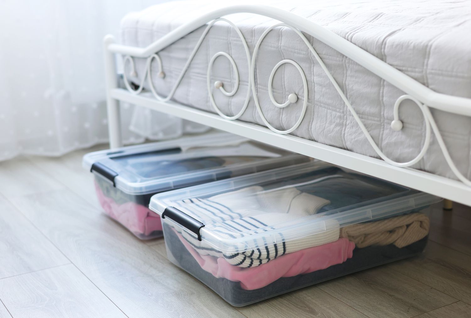 Plastic storage boxes filled with clothing under a metalframed bed