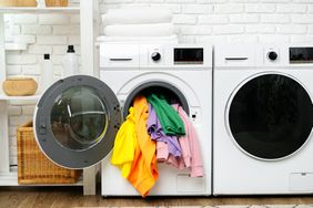 Frontloading washing machine with colorful clothes spilling out next to a matching dryer in a laundry room setup