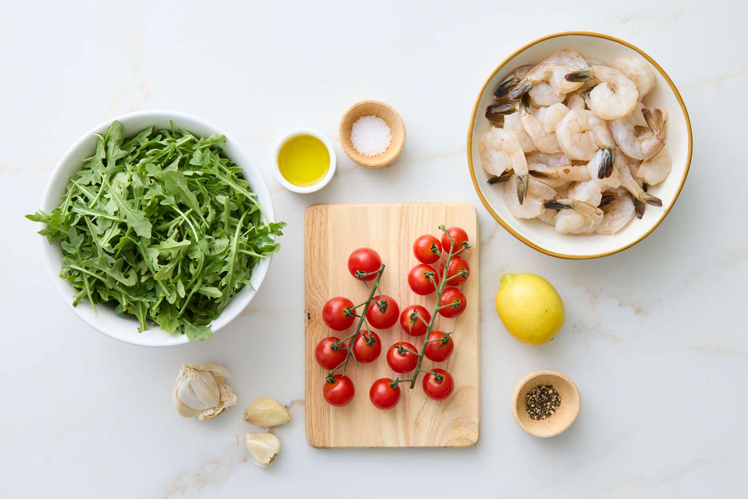 Preparation ingredients including shrimp, arugula, tomatoes, lemon, garlic, oil, and spices arranged on a surface