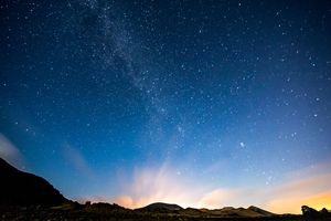 Starry night sky with a luminous horizon over silhouetted mountains