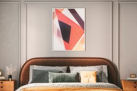 A neatly made bed with decorative pillows flanked by wooden side tables under a framed abstract artwork on the wall above