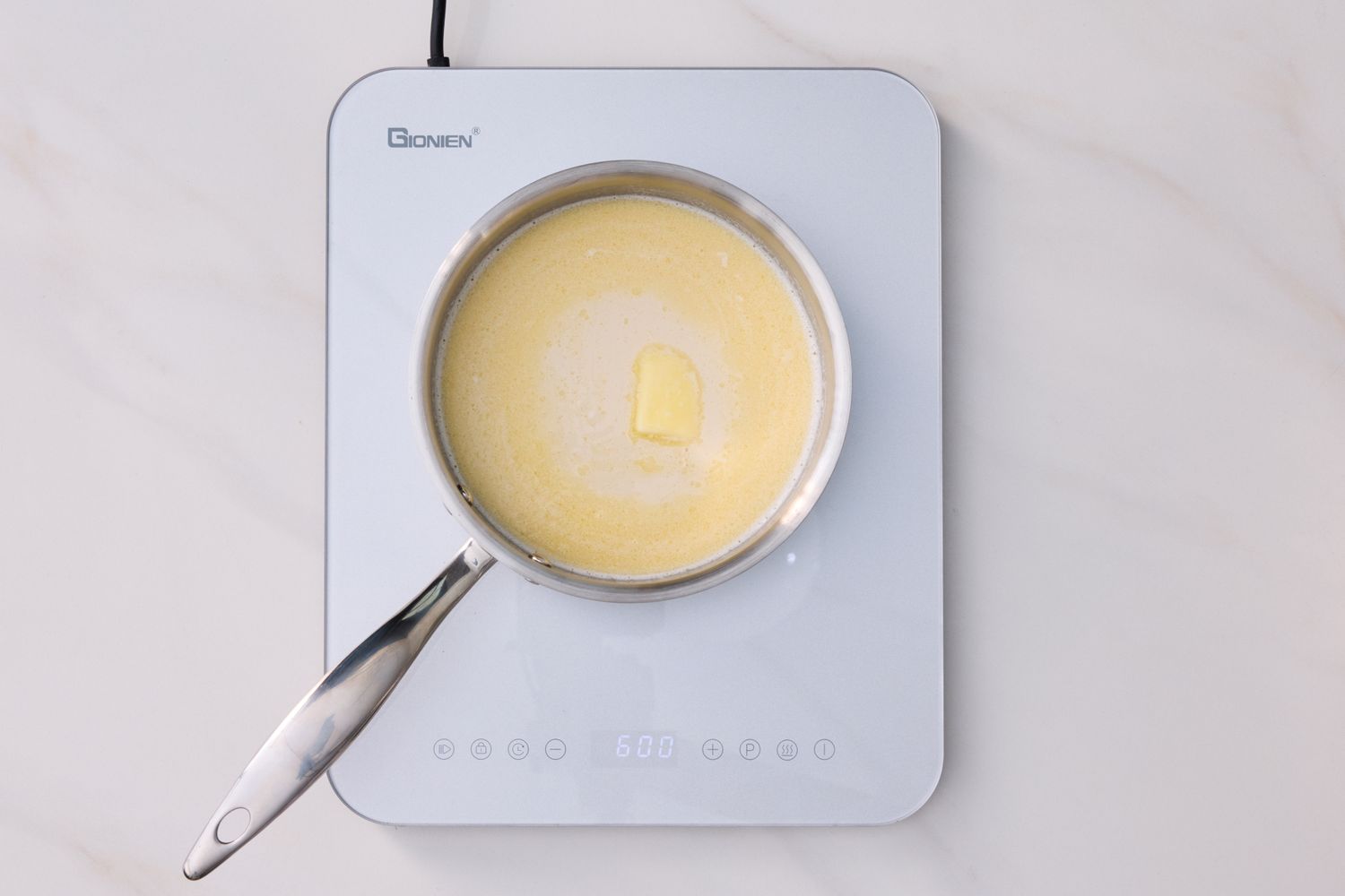 A pot containing a creamy mixture with a pat of butter on an electric stovetop