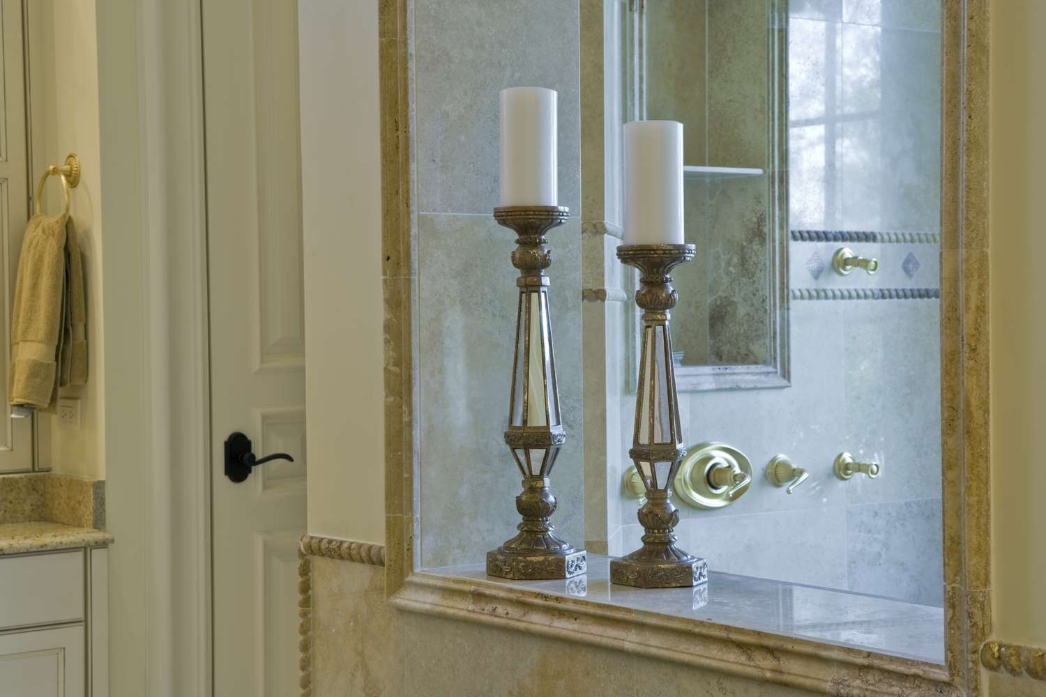A bathroom countertop with candle holders in front of a mirror and a glass shower enclosure in the background