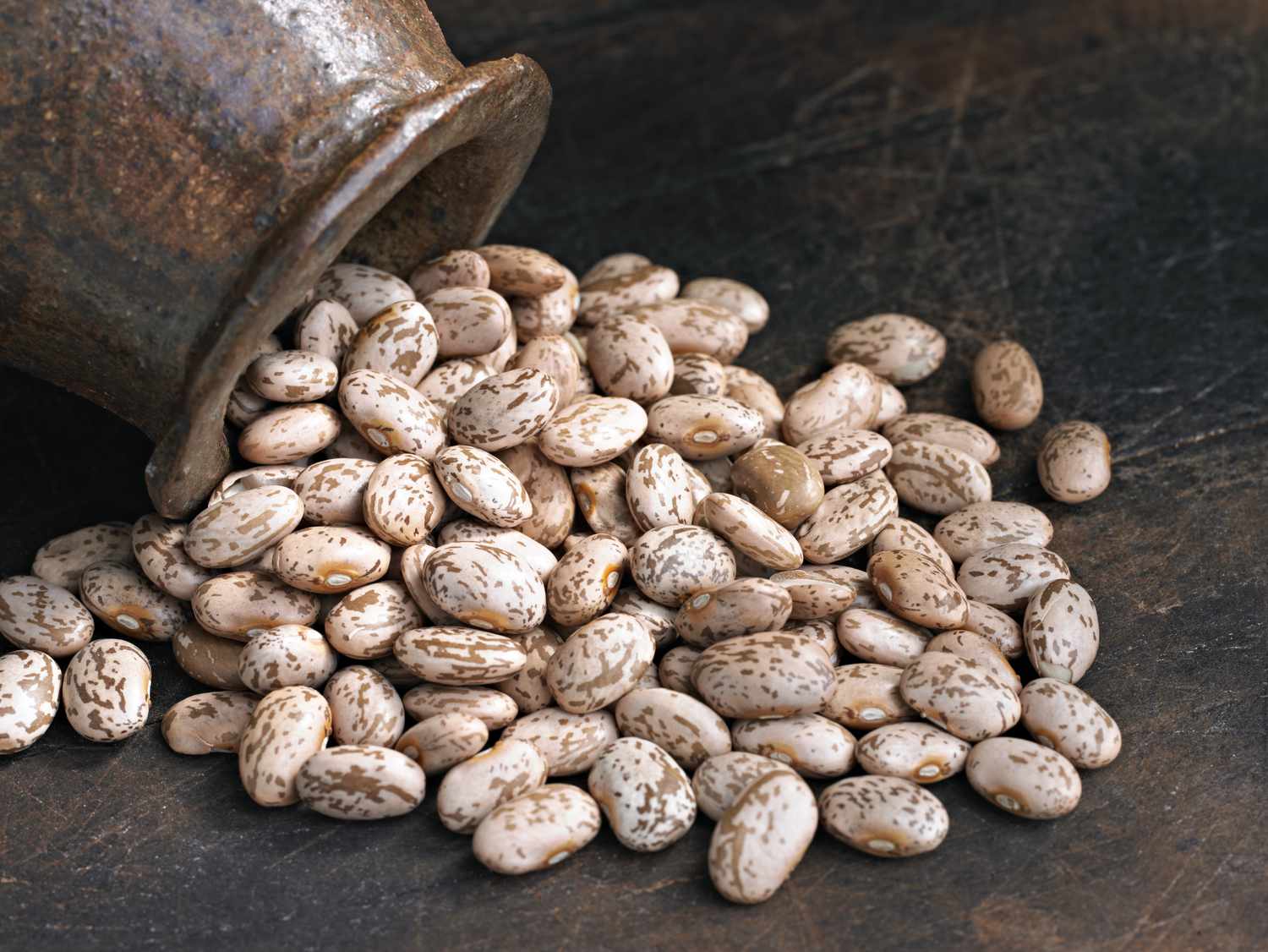dry pinto beans being tipped out of a heavy ceramic pot onto a surface