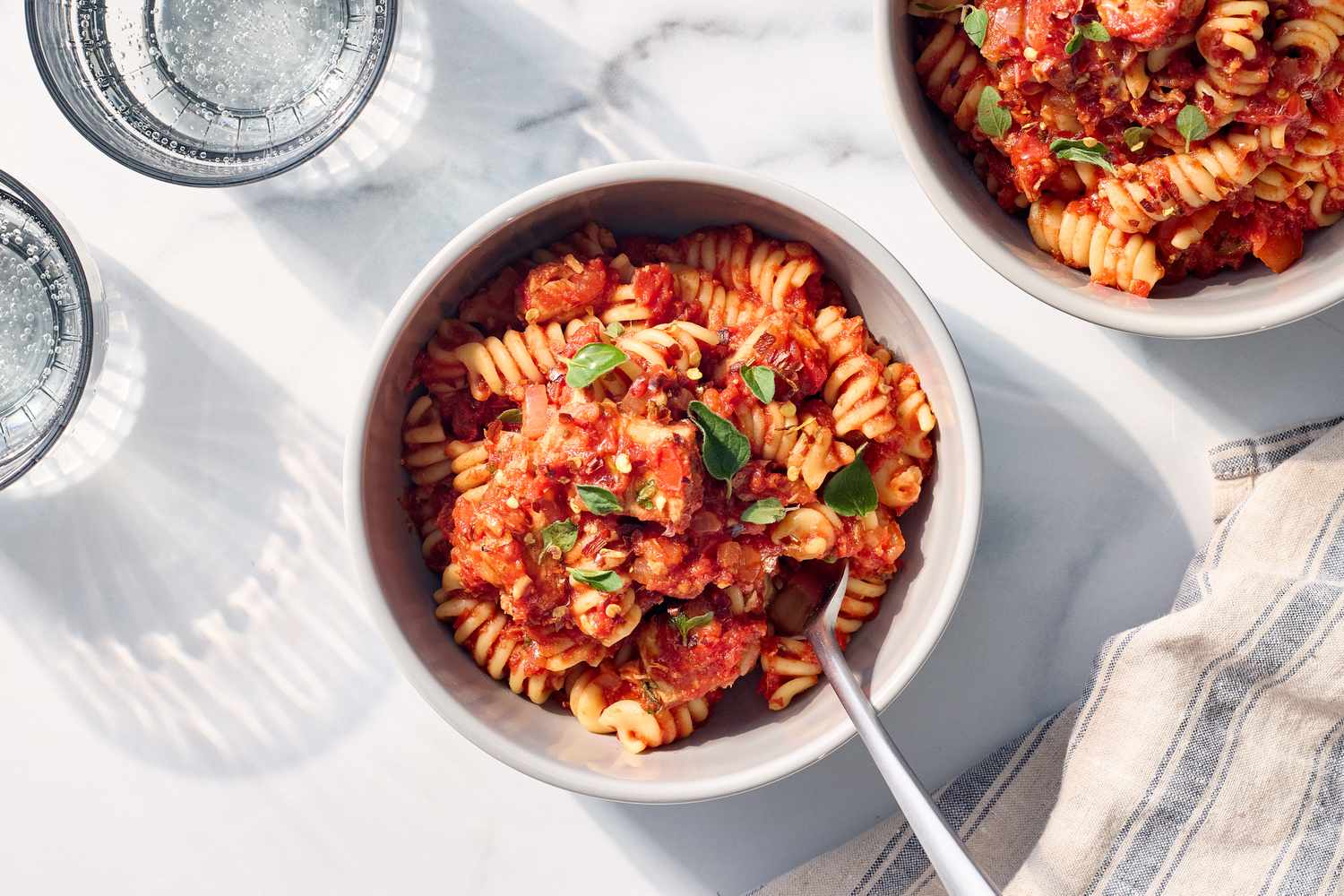 A bowl of pasta with a tomatobased sauce and garnish served next to glasses of water