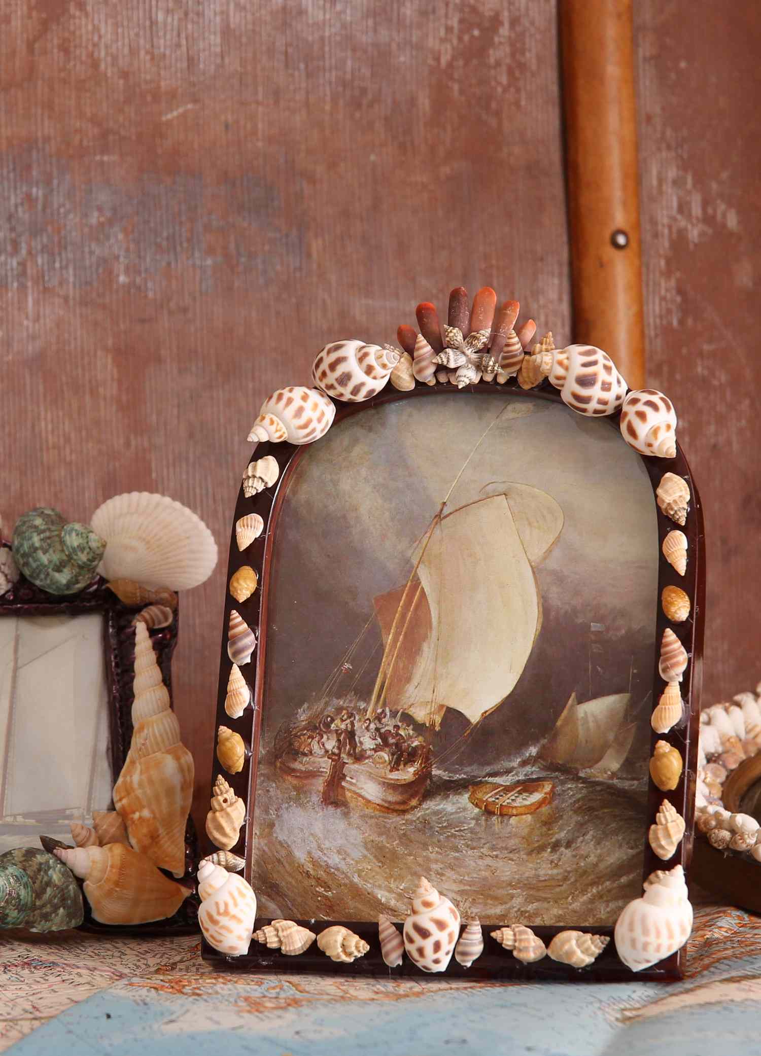 A seashell-framed artwork depicting a sailing ship in a stormy sea, surrounded by decorative shell arrangements