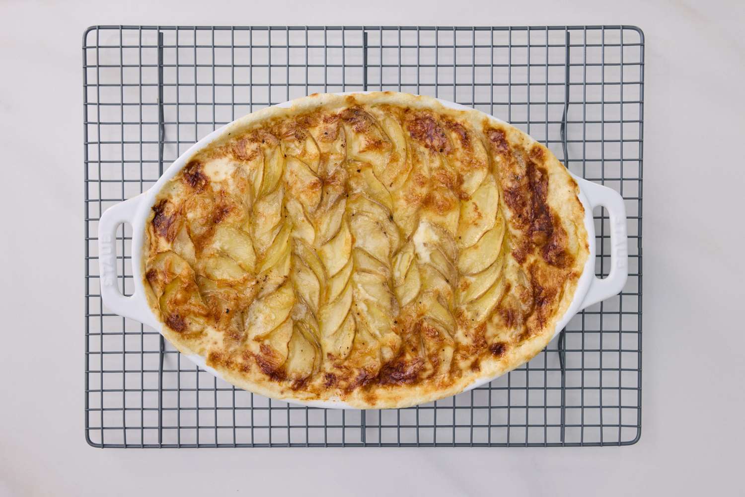 Scalloped potatoes in a white casserole dish resting on a cooling rack