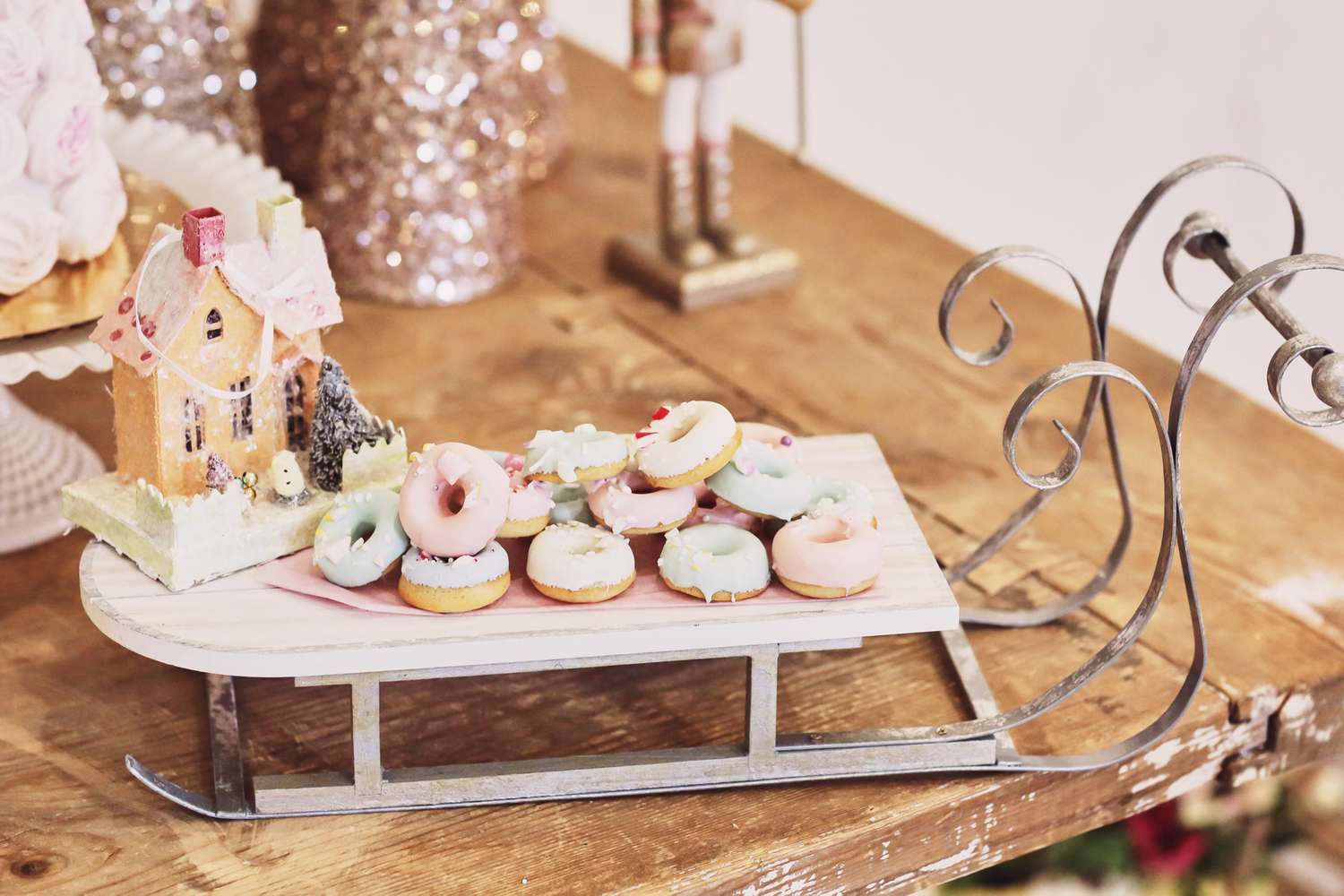 A decorative sled holding small pastries and a gingerbread house on a wooden table