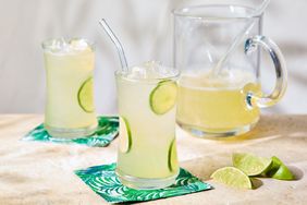 Two glasses of lime squash drink with ice next to a pitcher and lime slices