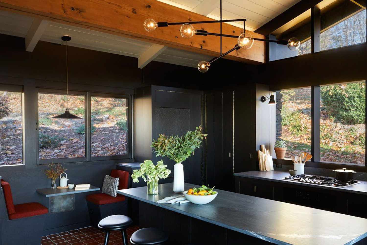 Modern kitchen with dark cabinetry large windows seating nook a countertop with bowls and pendant lighting