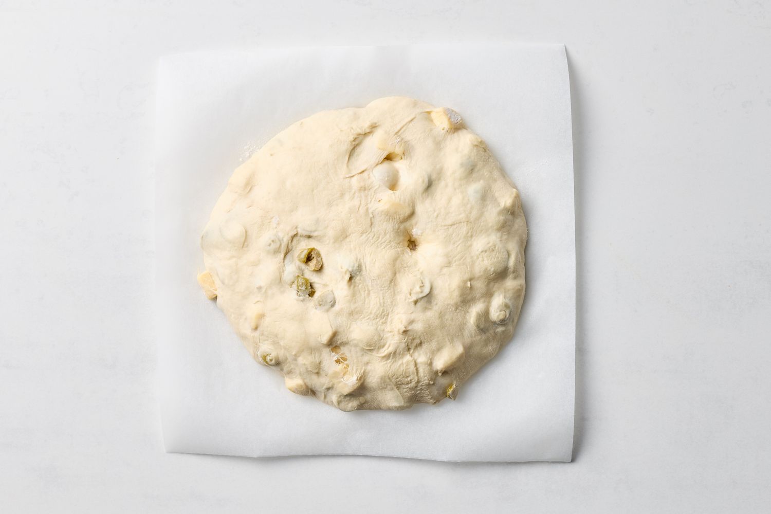 Unbaked round loaf of olive and cheese dough placed on parchment paper