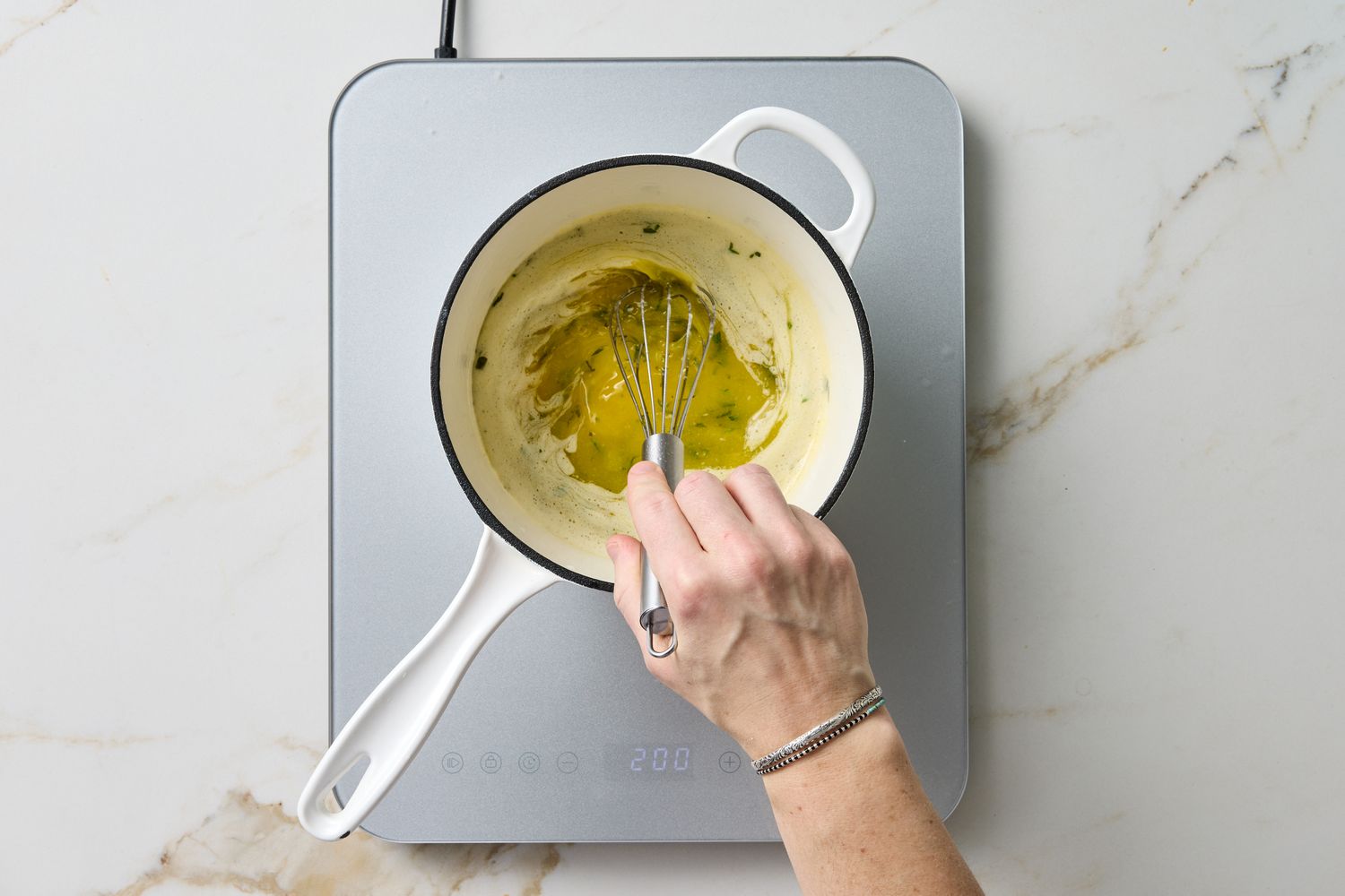 A hand whisking sauce in a saucepan on a stovetop