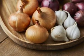 A wooden platter with onions garlic and shallots arranged together