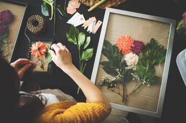 A person arranging pressed flowers in a frame on a table