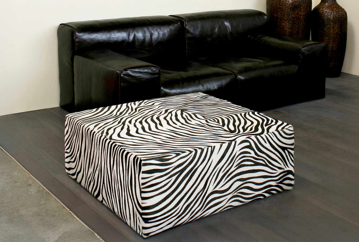 A zebrapatterned ottoman in front of a black leather sofa