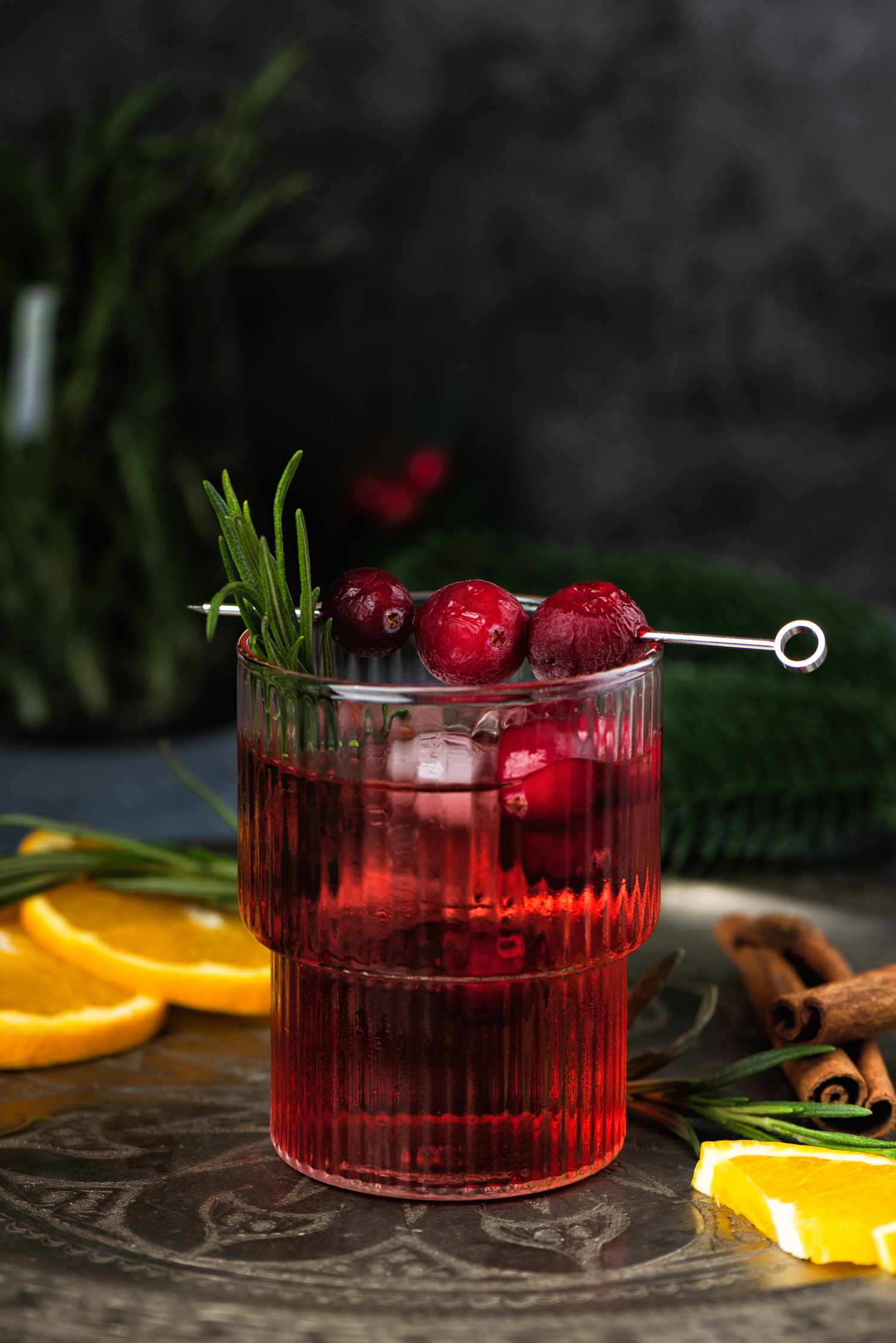 Cranberry boozy Christmas cocktail with ice and rosemary on dark background
