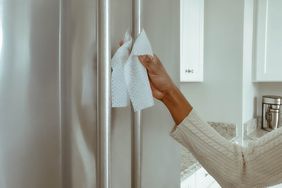 A person cleaning a refrigerator handle with a cloth