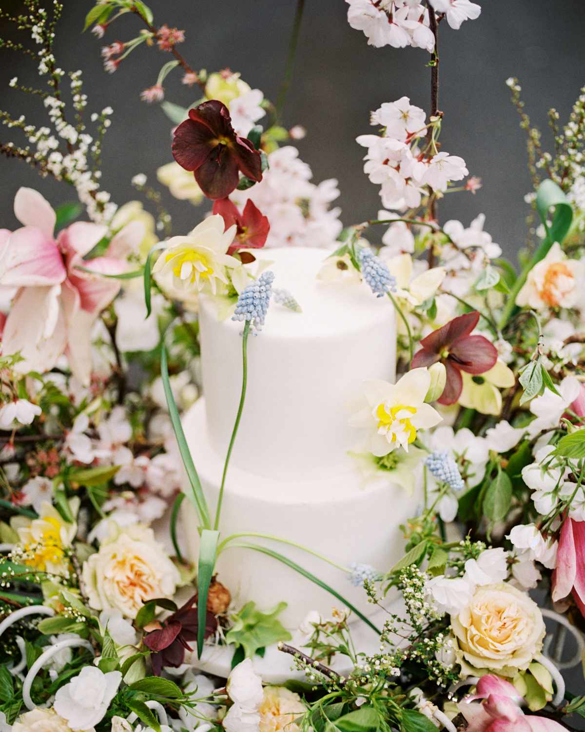 two tiered white frosted wedding cake surrounded by floral display