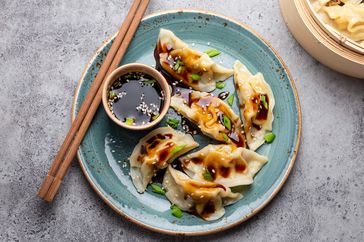 A plate of dumplings with dipping sauce and chopsticks