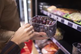 A person holding a container of grapes near a grocery store shelf