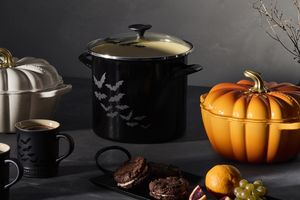 A collection of Halloweenthemed cookware and tableware including pumpkinshaped pots mugs and a decorative arrangement of food